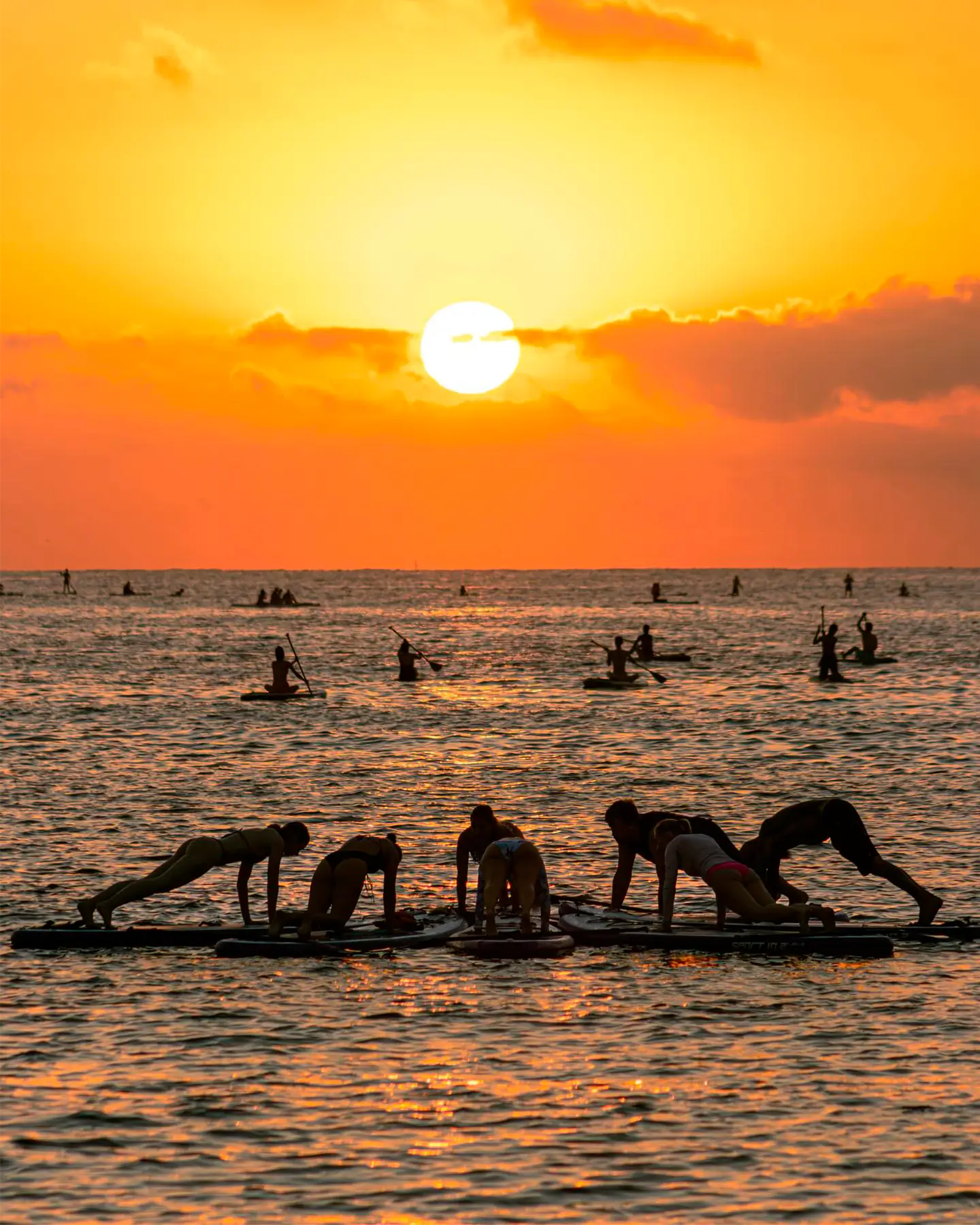 Grupo de personas practicando Paddle Surf en Barcelona en medio del amanecer.